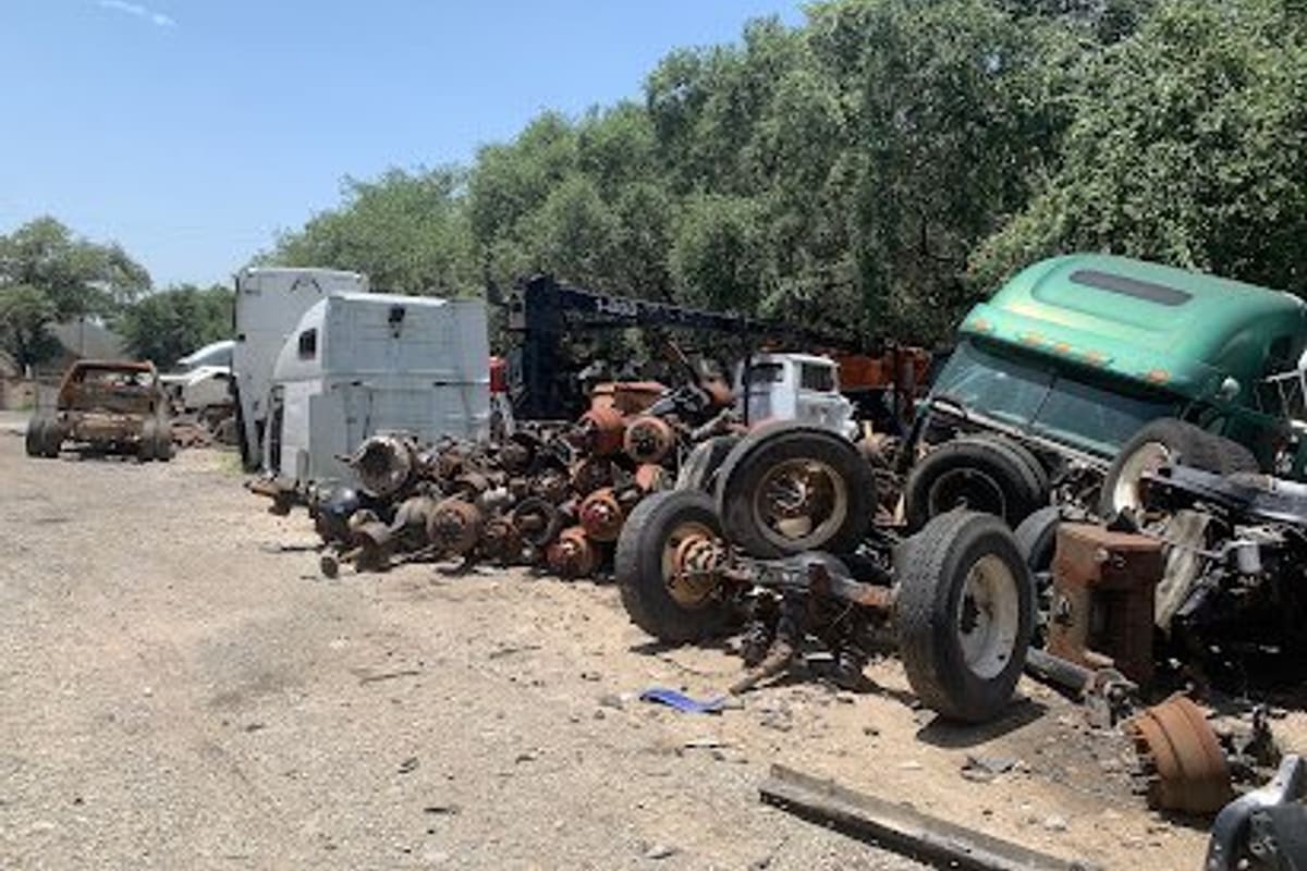 Southside Truck and Trailer: Gravel salvage yard with piles of truck axles, wheels and dismantled semi cabs under a clear sky with trees behind