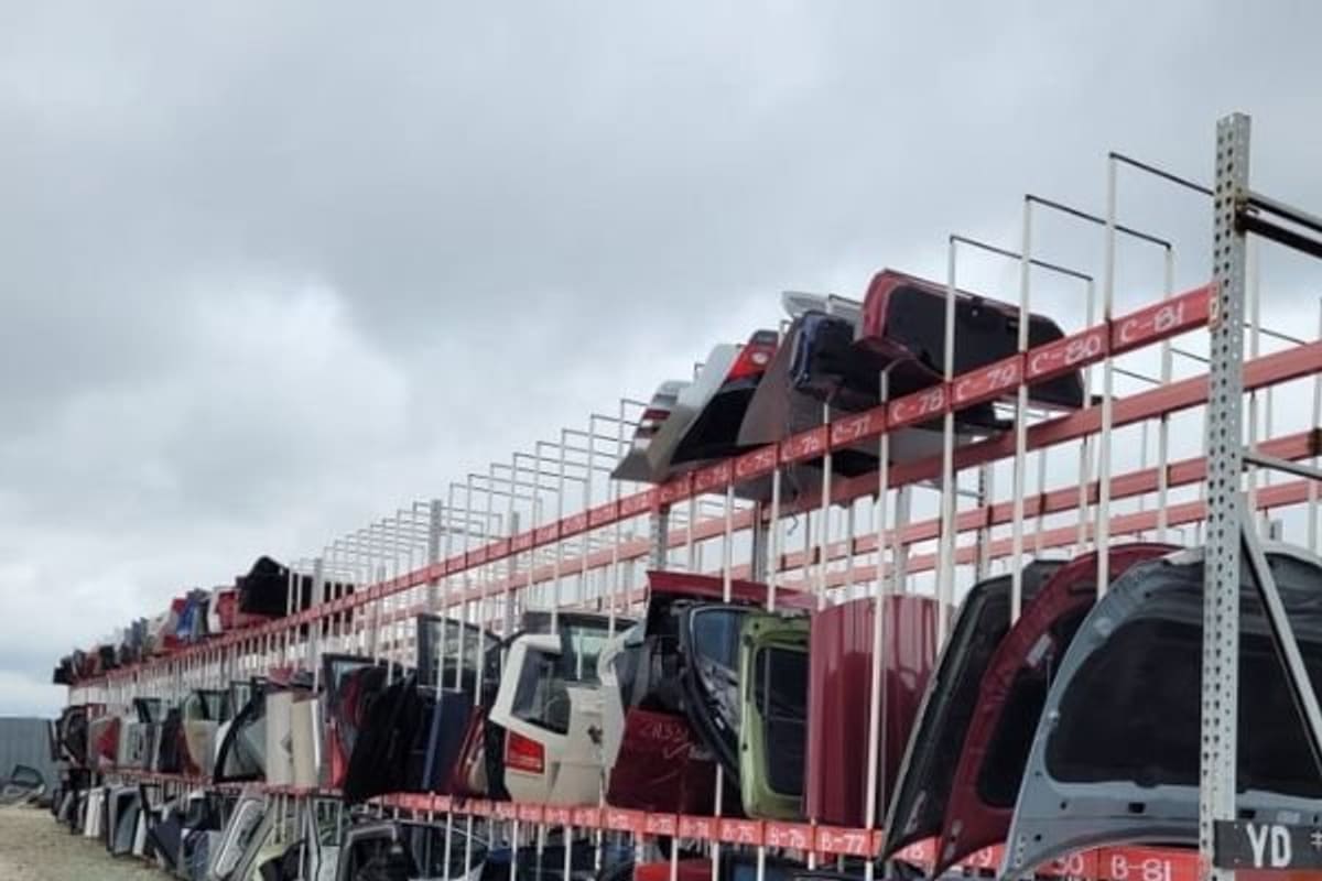 Giant Imports Junkyard: Tall red racks of used car doors and hoods lined up along a gravel lane in an outdoor salvage yard under a cloudy sky