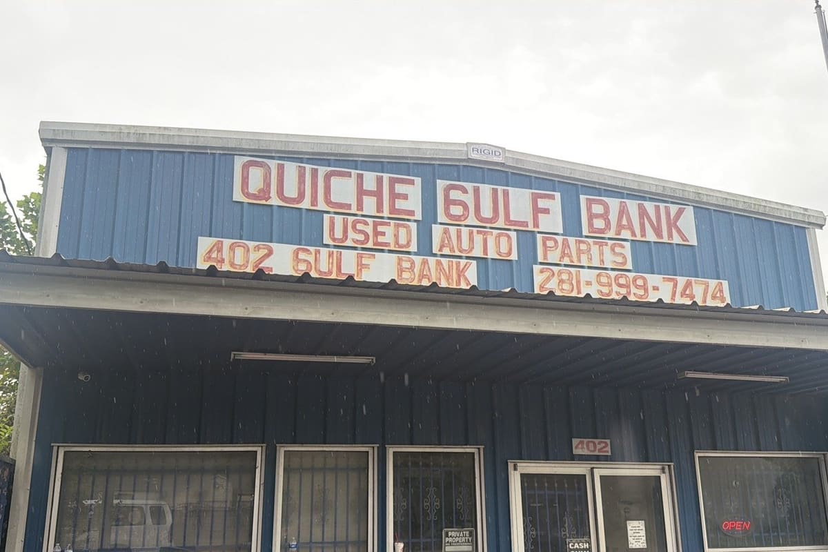 Gulf Bank Used Auto Parts: Blue metal building with hand-painted signs reading used auto parts, a phone number, and address 402, with barred windows and glass doors