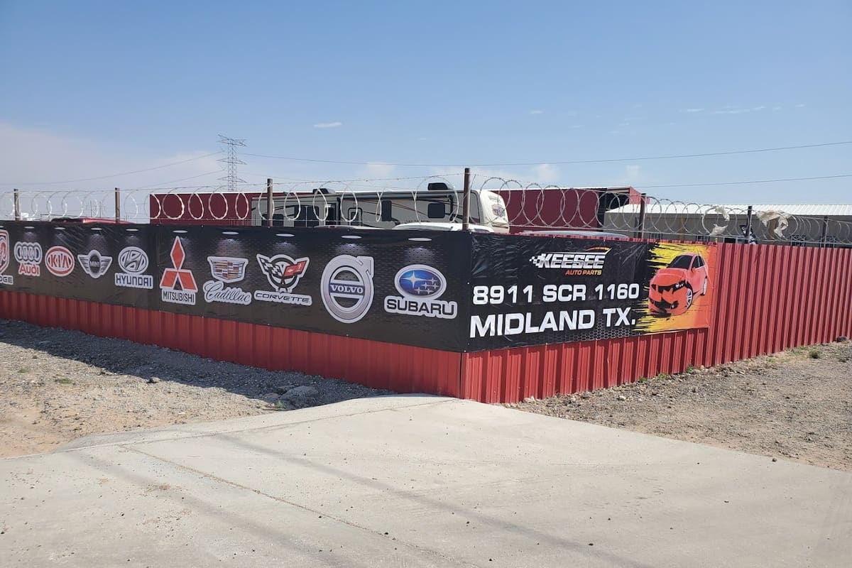Keesee Auto Parts: Red metal fence with a large banner of car brand logos and a Midland, TX address, topped with razor wire