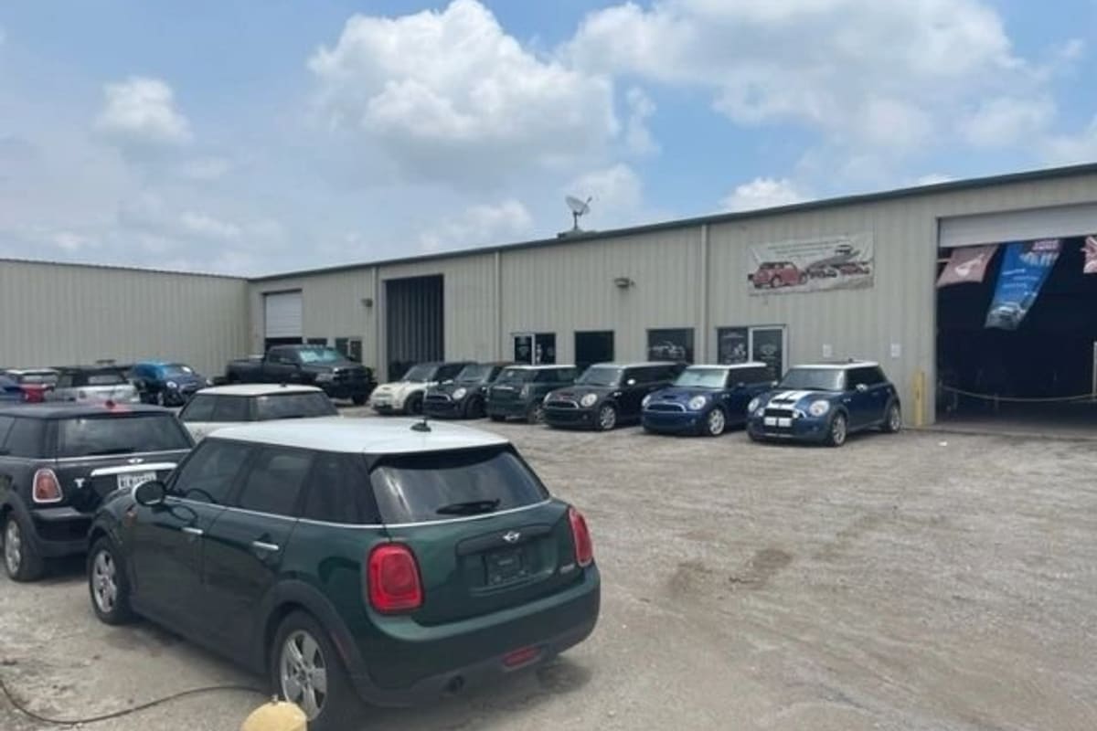 Open Road Mini Parts and Service: Rows of Mini Cooper cars parked on a gravel lot in front of a metal warehouse building with open bay doors