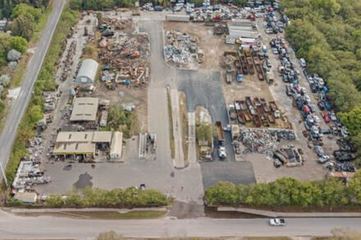 Guaranteed Auto and Truck Parts: Aerial view of a salvage yard with rows of vehicles, scrap piles and several buildings beside a road