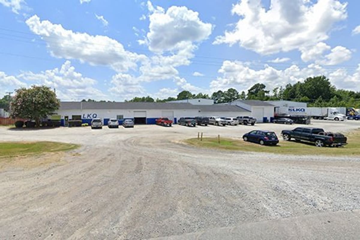 LKQ East Carolina: Wide gravel lot in front of a long white auto salvage building with parked cars and trailers