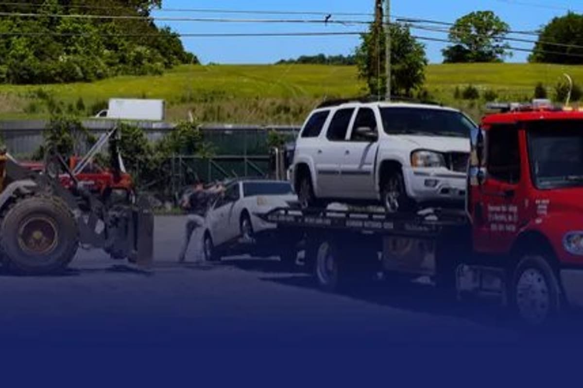 Tas Recycling: Yellow wheel loader, tow trucks carrying cars and a large scrap pile on a gravel lot beside a grassy hill