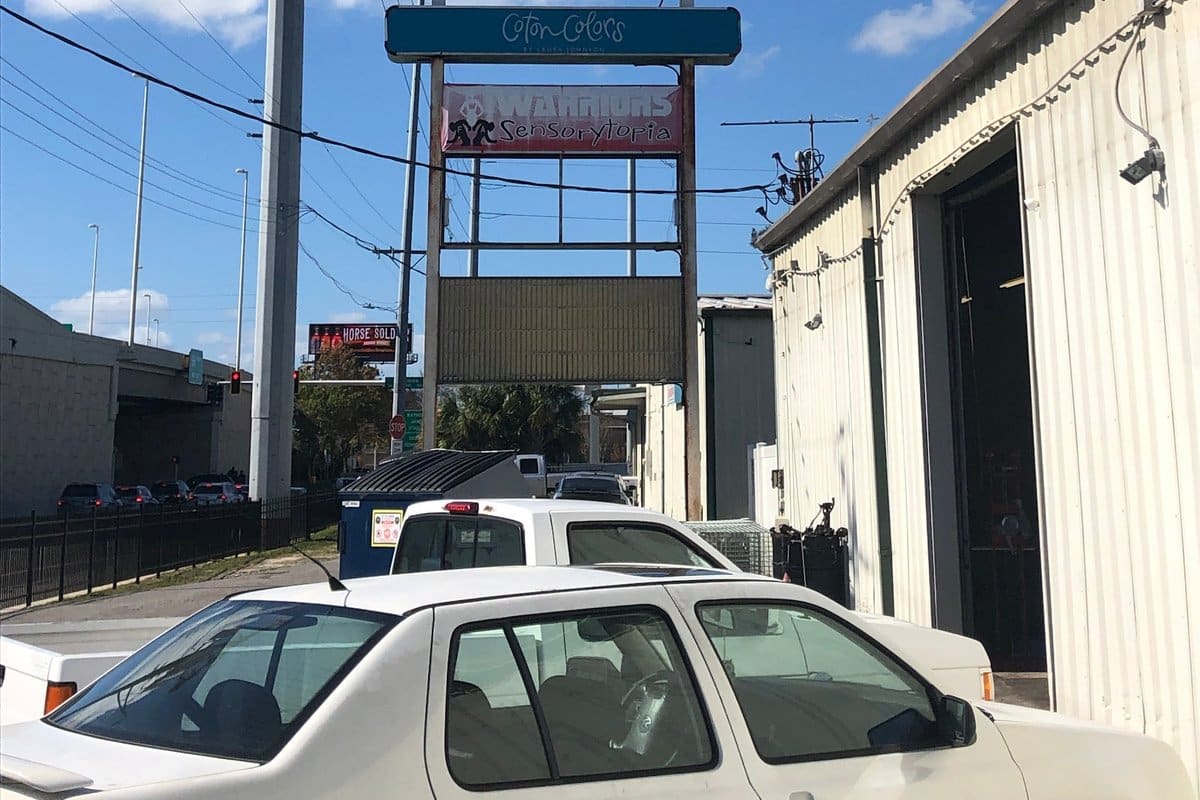 Allmag Auto Parts: Tall roadside pole sign for an auto parts store beside a metal warehouse building under a blue sky