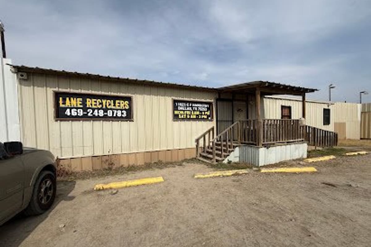 Lane Recyclers: Tan modular office building with black signs, a covered wooden porch with steps, and a gravel lot with yellow curbs