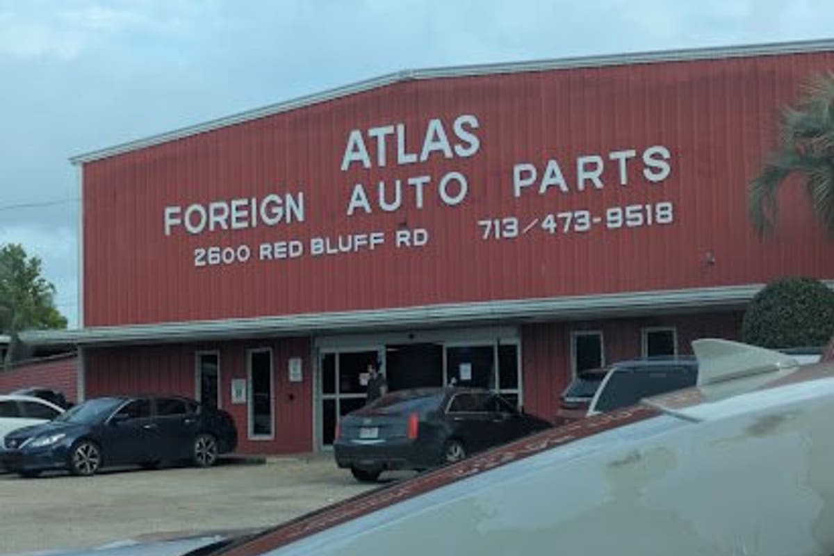 Atlas Foreign Used Auto Part: Red metal warehouse building with large white lettering on the front, a street address and phone number, and cars parked outside