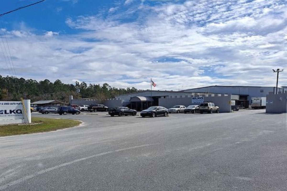 LKQ North Florida: Wide view of an auto parts facility with a roadside sign, gray warehouse buildings, and cars parked in the front lot