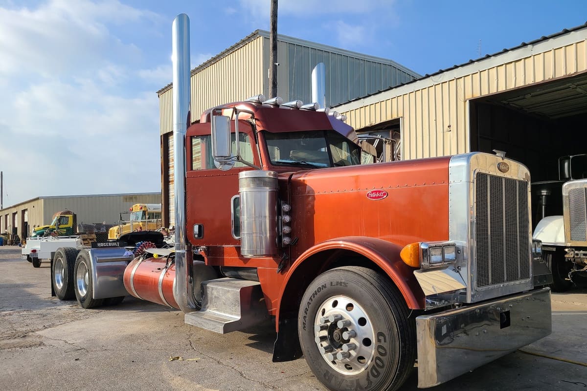 Rose Sales: Red semi truck parked on a concrete lot in front of metal shop buildings, with other vehicles in the background