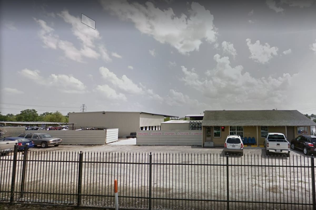 A-Plaza Auto Parts #2: Wide daytime view of a fenced salvage lot with parked cars, a low office building and a metal warehouse behind