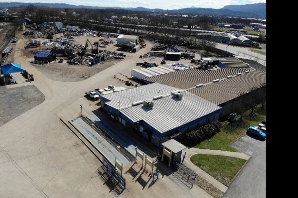 CMC Recycling: Aerial view of a metal recycling yard with a blue-roofed industrial building, scrap piles and a paved lot