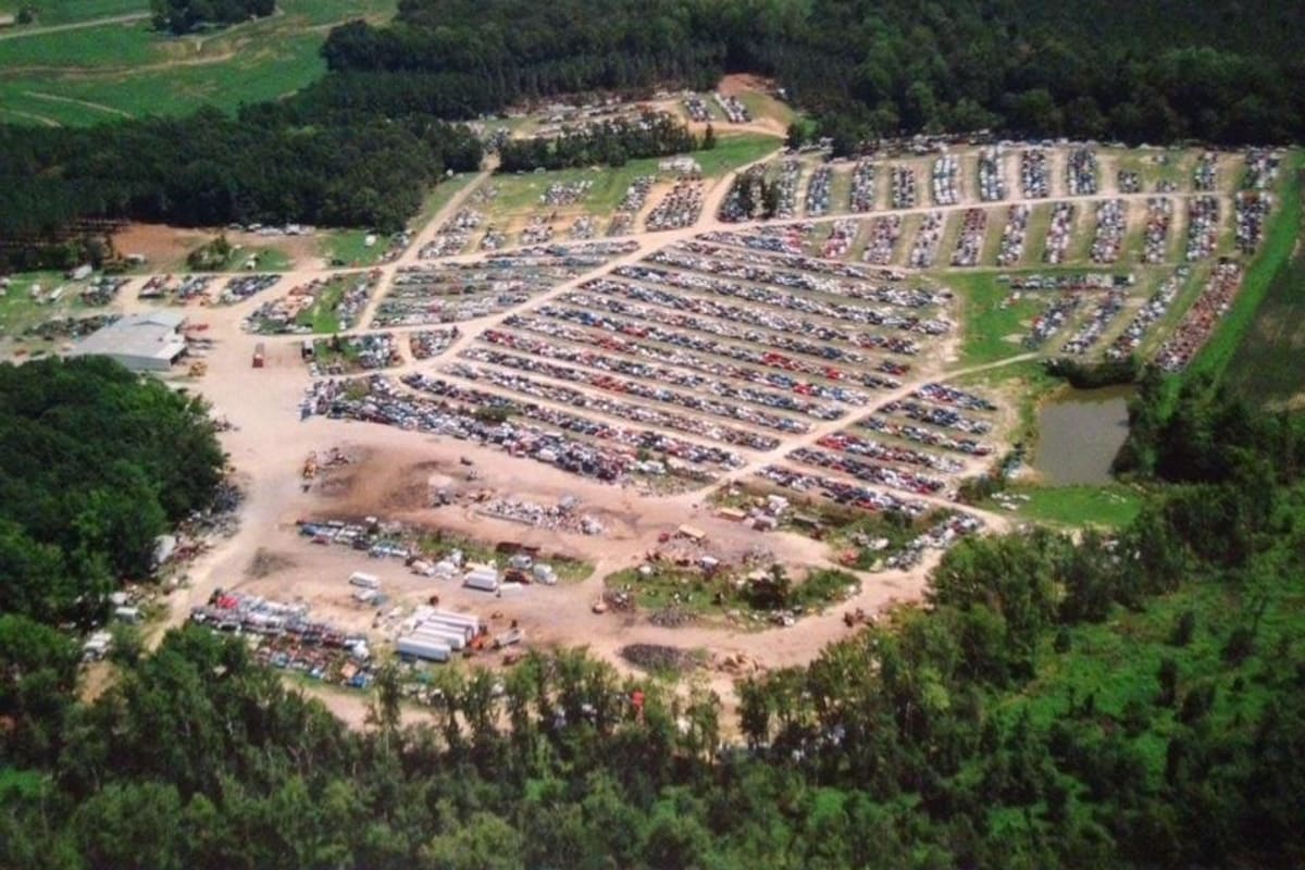 Cox Auto Salvage: Aerial view of a large salvage yard with long rows of vehicles, a dirt lot, a pond and surrounding forest