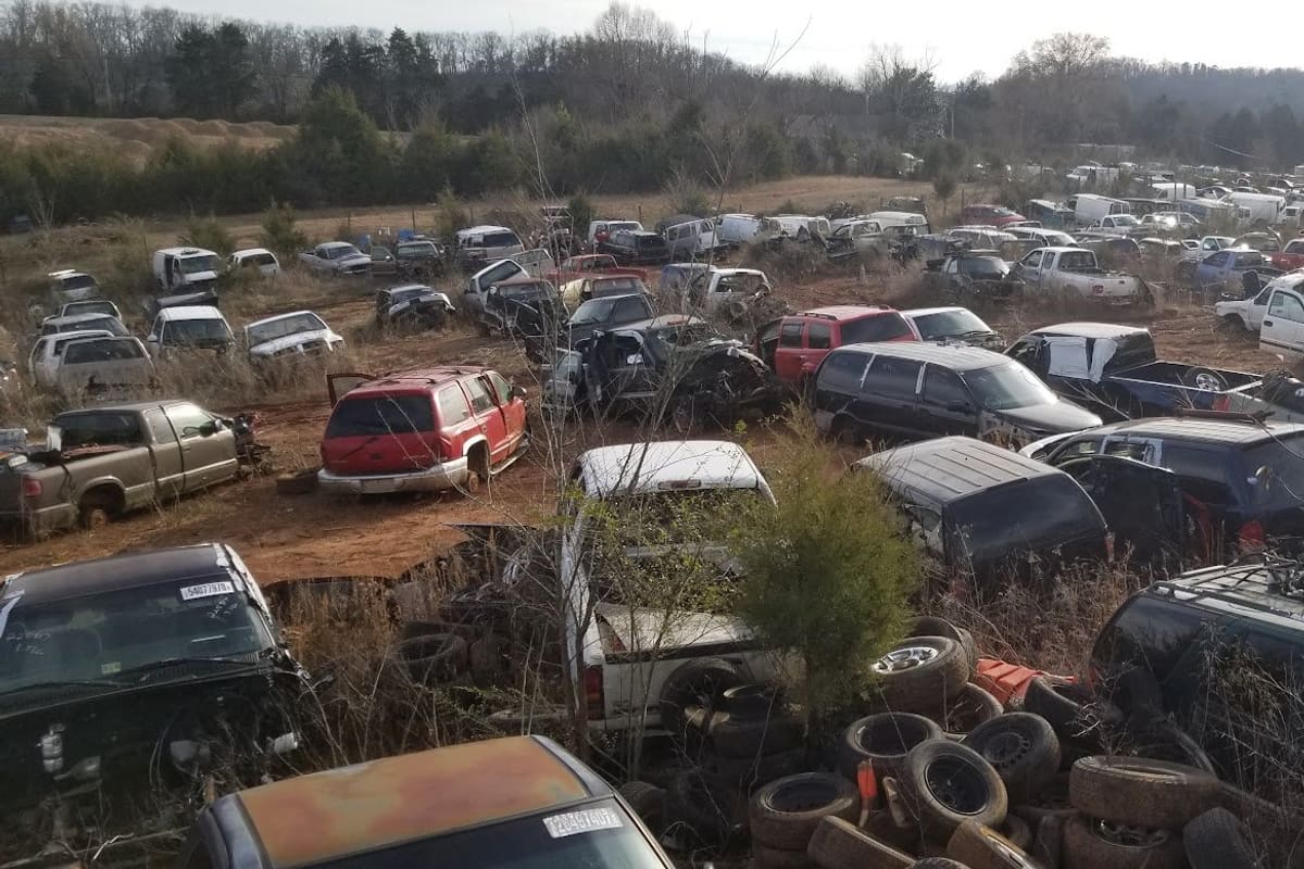 Jones(jasper) Auto Parts: Wide view of a salvage yard with rows of old cars, trucks and a pile of tires on red dirt ground