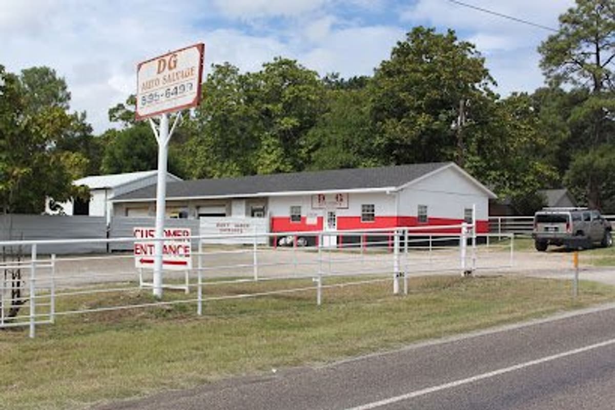 DG Auto Salvage: White and red office building behind a white pipe fence, with a roadside sign and customer entrance sign out front