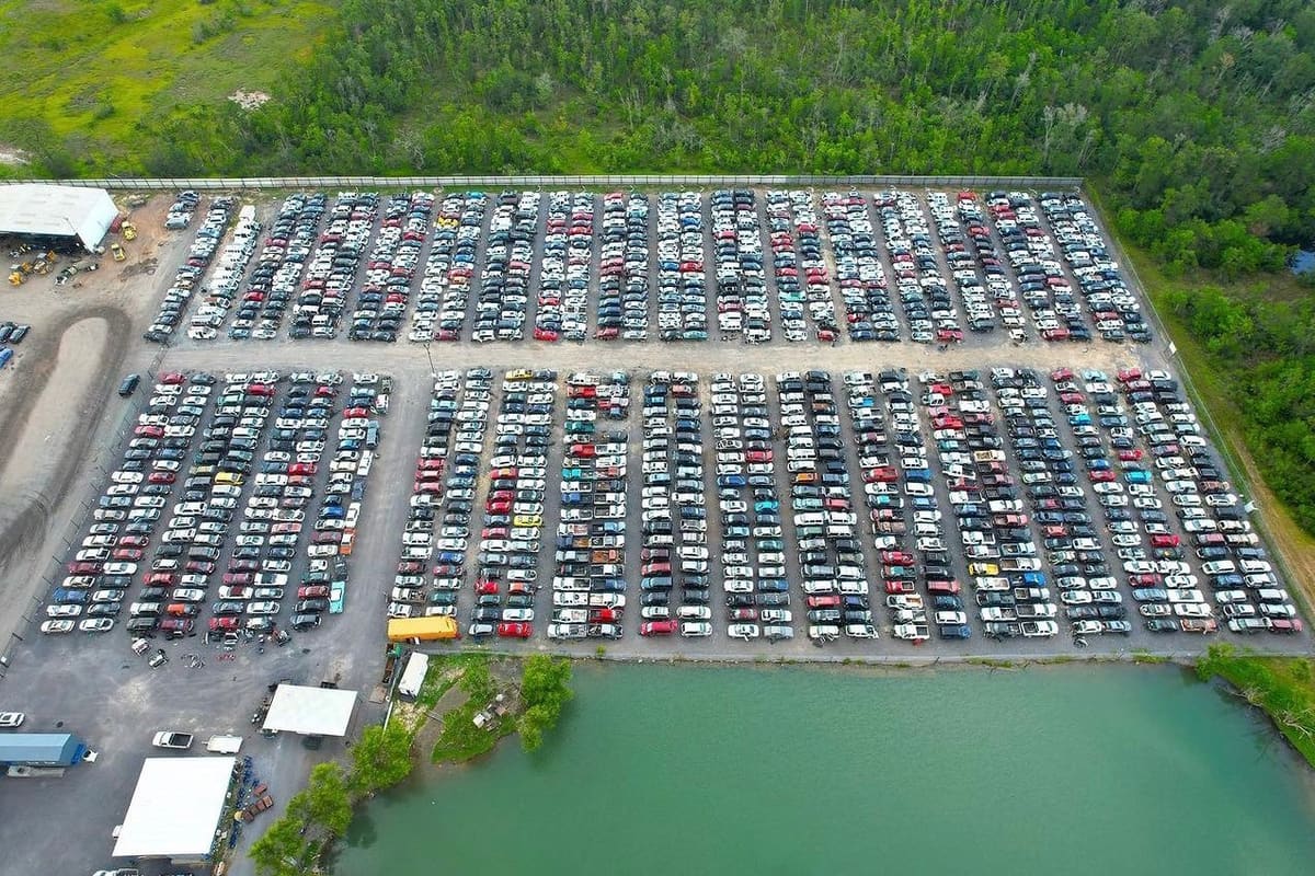 Prestige Pull Your Part: Aerial view of a large salvage yard with long rows of vehicles parked beside a green pond and trees
