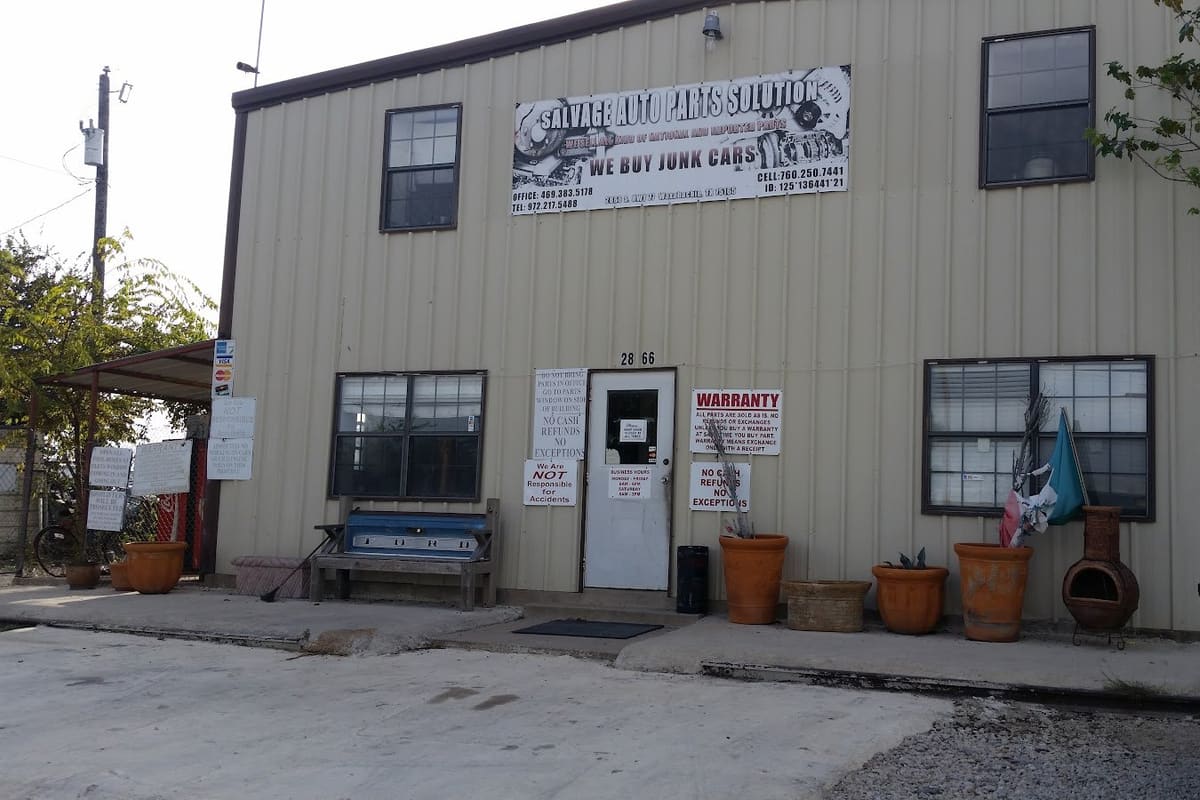 Salvage Auto Parts Solution: Two-story tan metal building with a large salvage parts sign above the door, planters, a bench and warning notices