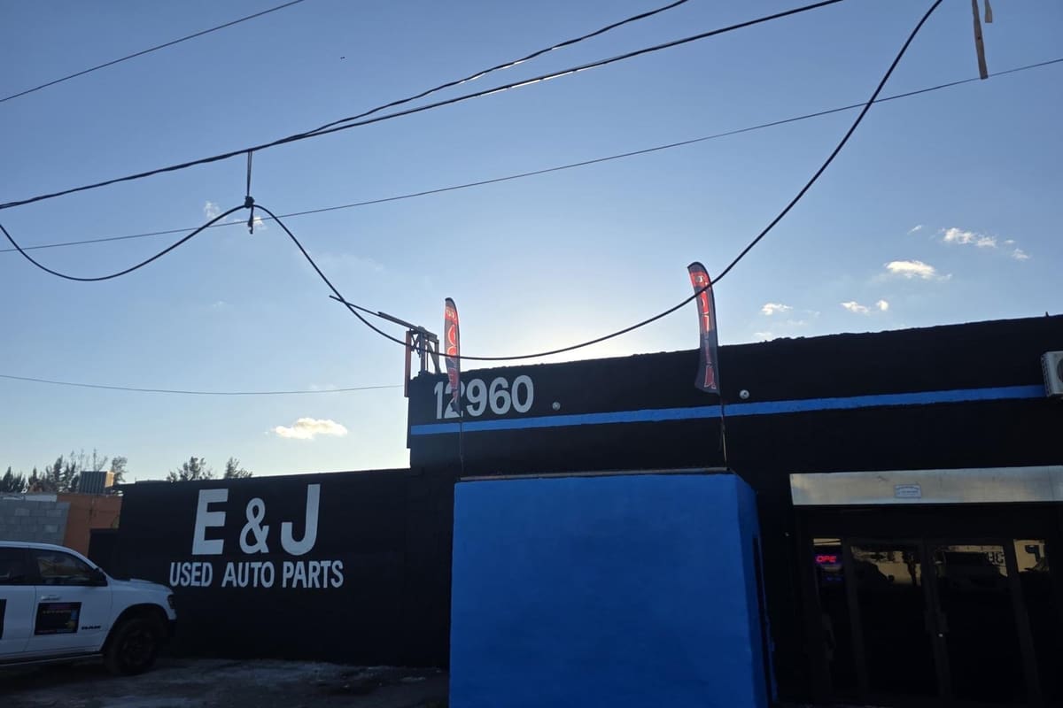 EJ Opa Locka 2: Black used auto parts building with street number 12960, a blue accent stripe and a white pickup parked out front
