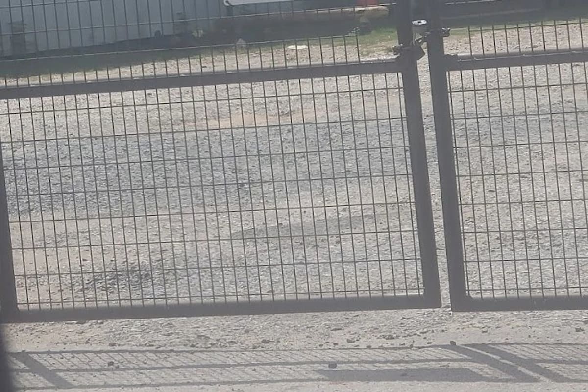 Andy's U-Pull It: Locked wire gate with a posted hours sign in front of a gravel lot and a small building with a red door marked Enter