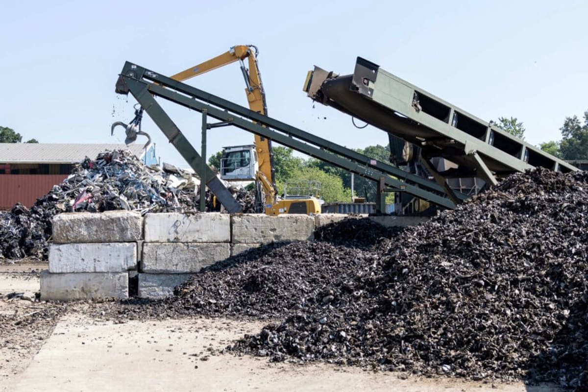 CFC Recycling: Scrap metal yard with conveyor stacker, material handler crane, and piles of shredded metal behind concrete blocks