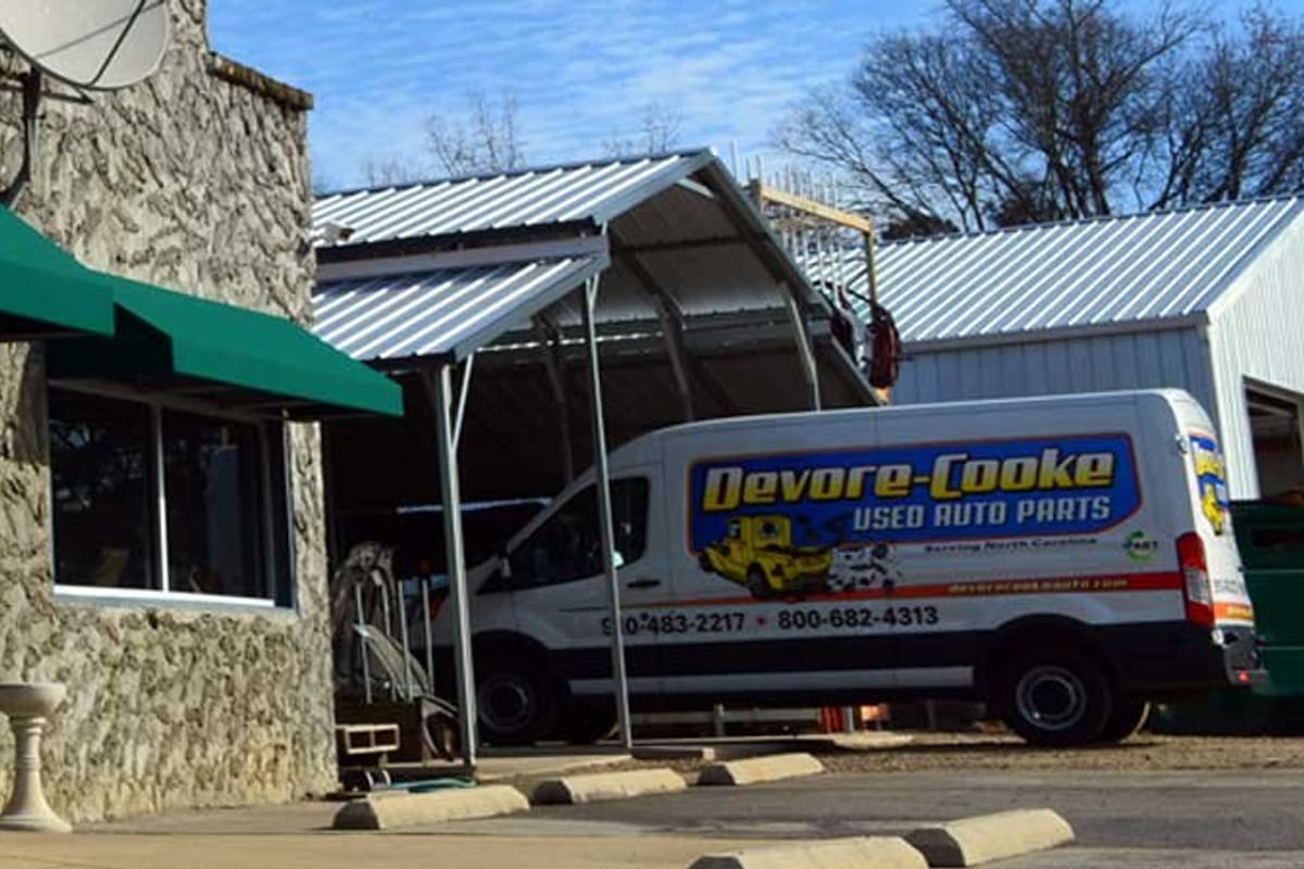 Devore and Cooke Auto Parts: Stone-faced building with green awning over glass entrance, number 1529, and a parts van parked beside a metal carport