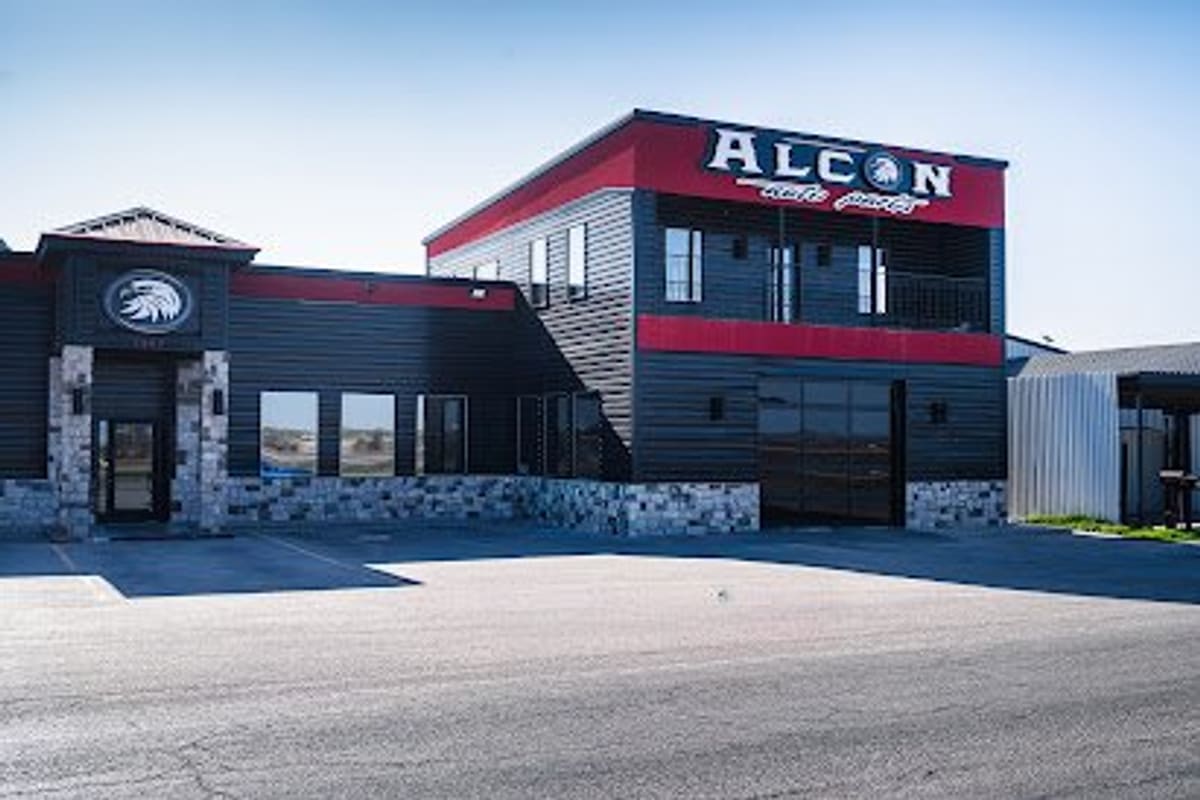 Alcon Auto Parts: Two-story black and red building with stone accents, an eagle emblem, and a large sign above a paved parking lot