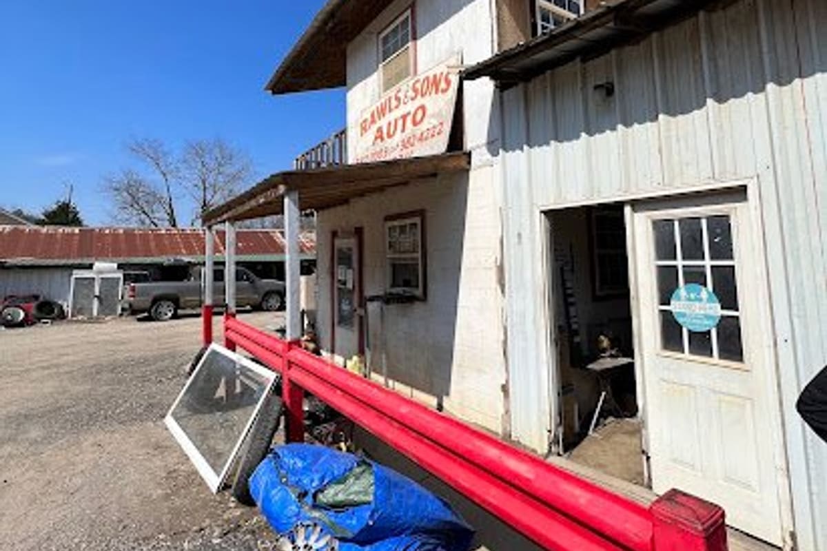 Rawls and Son Auto: Two-story white wooden building with a red railing, a hand-painted auto sign, and a gravel lot under a clear blue sky