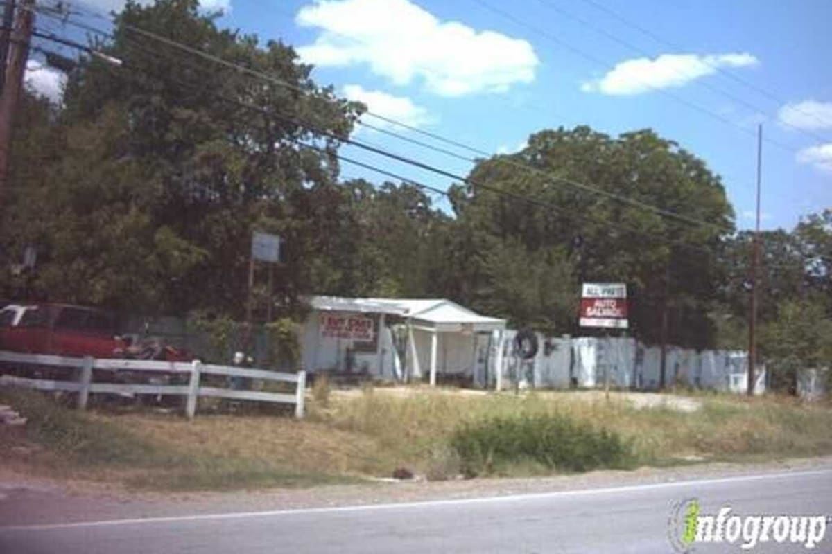 Affordable Auto Salvage & Recycling Center: Small white roadside shop with a covered entrance, an auto salvage sign and a fenced yard behind a white wooden fence