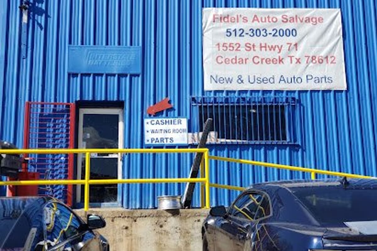 Fidels Auto Salvage: Blue corrugated metal building with a banner sign for new and used auto parts and a cashier and parts entrance