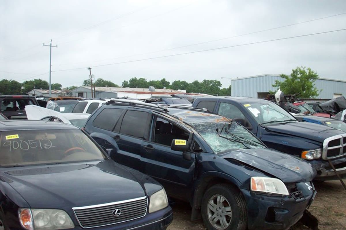 United Foreign Auto & Truck Parts: Rows of wrecked cars and SUVs parked on a gravel salvage lot under an overcast sky, with metal buildings behind
