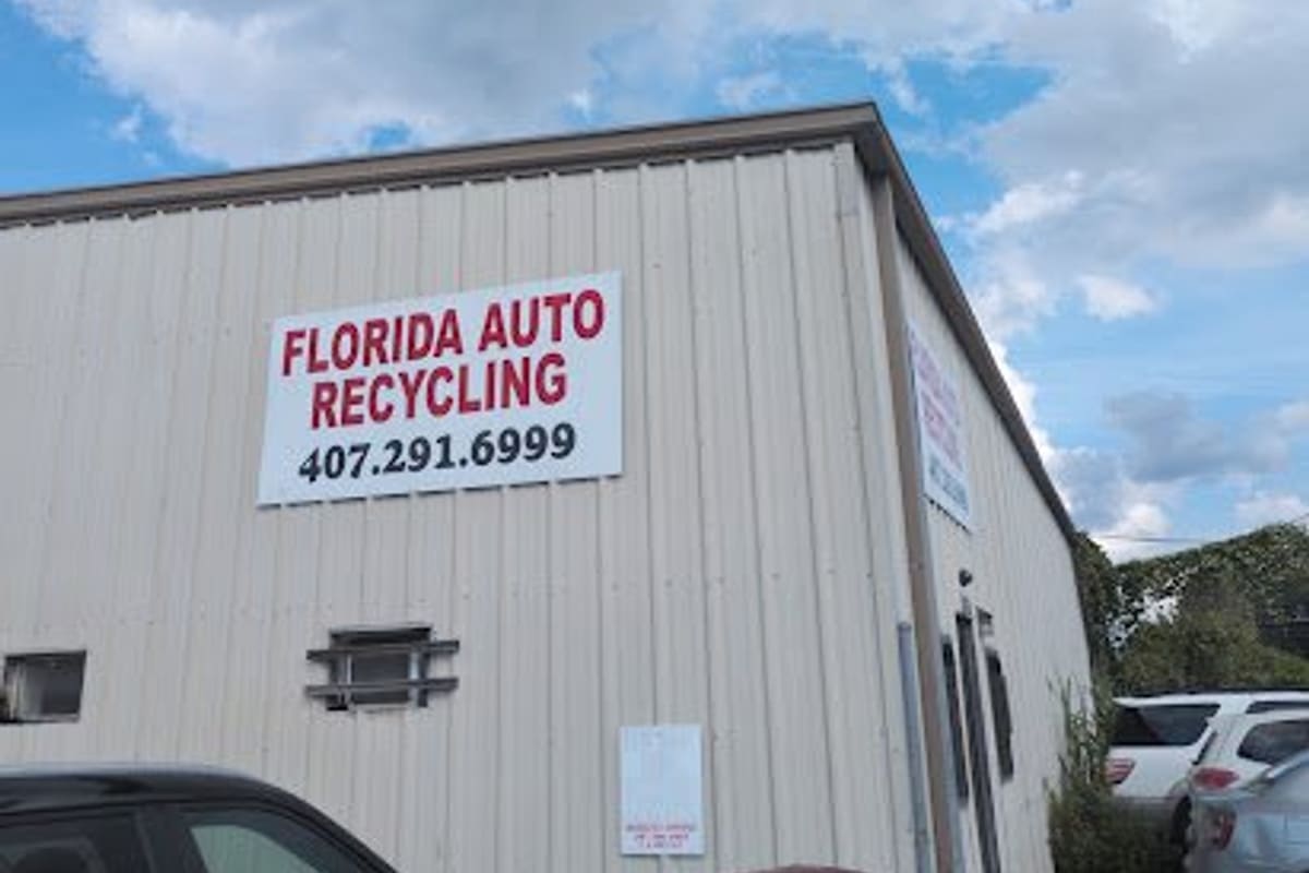 Florida Auto Recycling: Tan metal warehouse building with a large red and white sign and phone number, cars parked in front under a cloudy sky