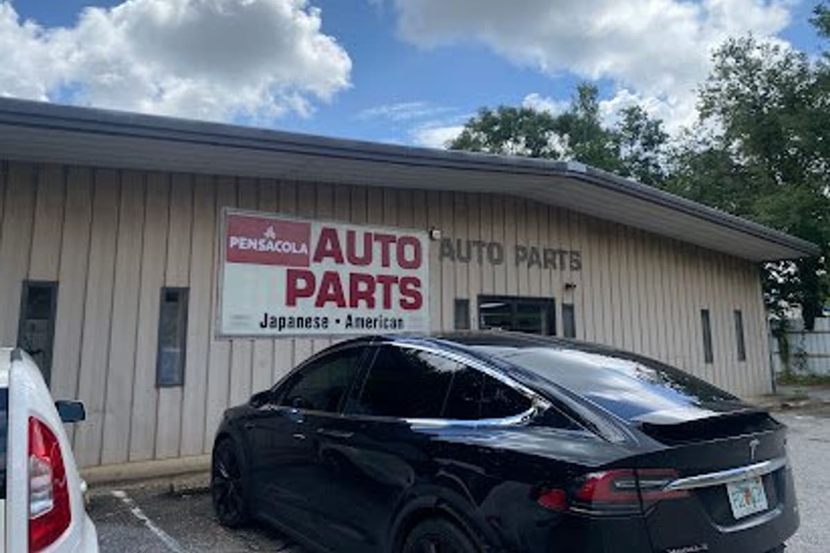 Pensacola Auto Parts: Tan single-story auto parts store with a large red and white sign and cars parked in front under a blue sky