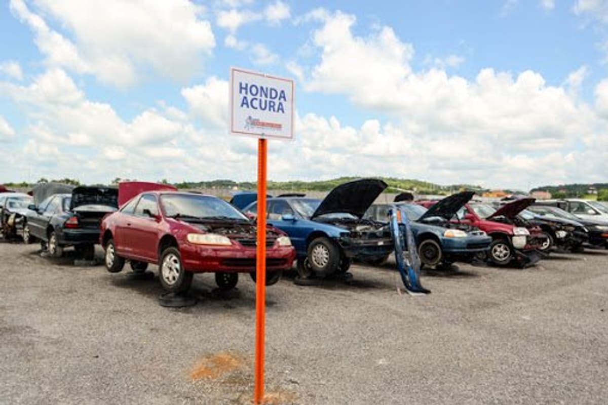 A & C Auto Parts: Rows of salvage Honda and Acura cars with open hoods on a gravel lot beneath a cloudy blue sky