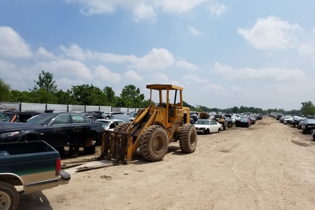 Star Auto Parts: Yellow front loader on a dirt lane beside rows of salvage cars under a partly cloudy sky