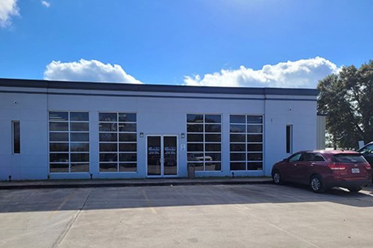 LKQ West Florida: Single-story gray commercial building with large grid windows, glass double doors, and a paved parking lot