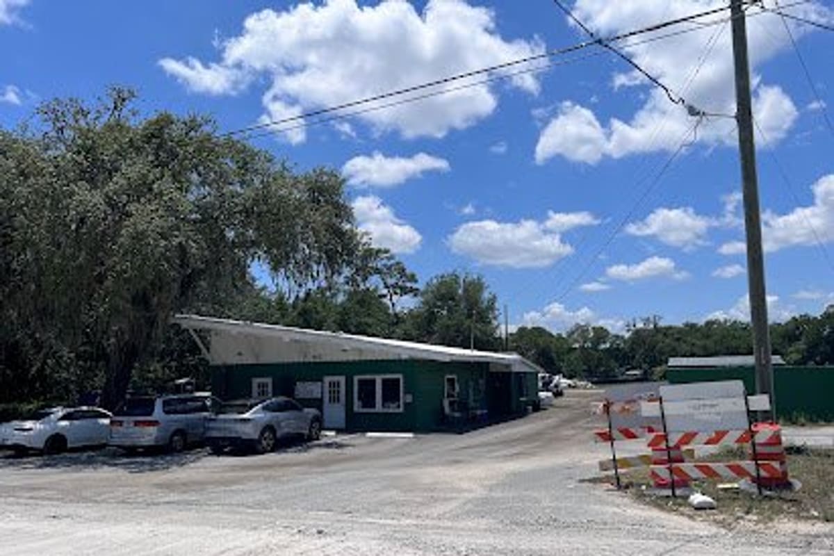Lady Lake Auto Salvage: Green single-story office building with cars parked beside it on a gravel lot under a blue sky
