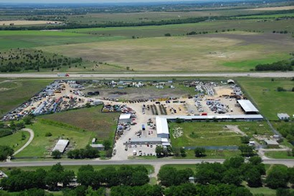 Frontera Truck Parts & Equipment: Aerial view of a large salvage yard with rows of vehicles, metal buildings and a paved lot beside a highway