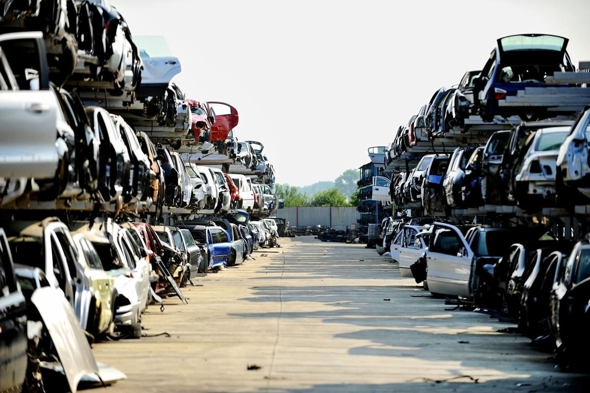 Flat Rock Auto Parts and Salvage: Long aisle between tall stacked rows of wrecked cars at a salvage yard under a clear sky
