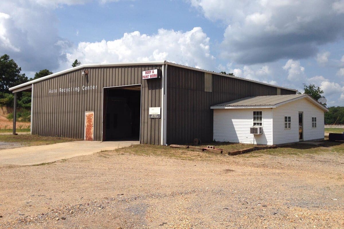 Karamwright Auto Salvage: Metal shop building with a large open bay door and a small white office building beside it, on a gravel lot