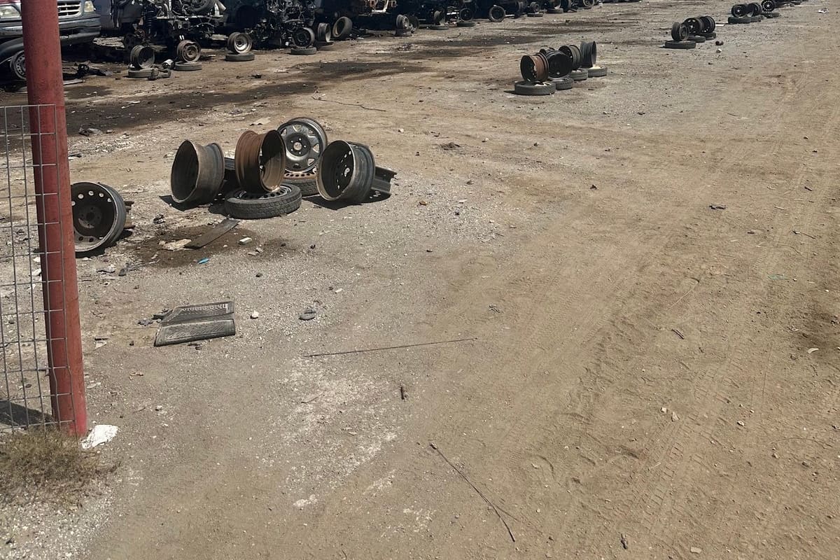 Roosevelt Wrench A Part: Wide view of a dirt salvage yard with rows of wrecked cars and piles of wheels under a blue sky