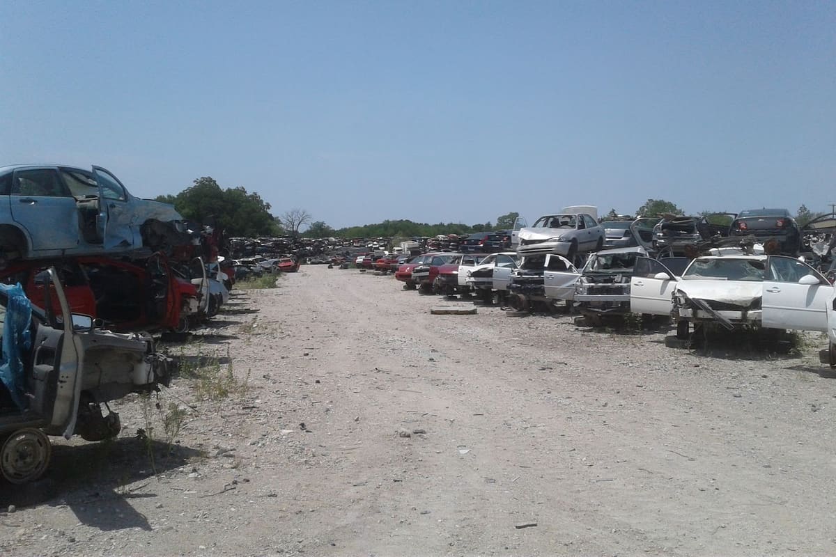 Dismantler's 2000: Dirt lane between rows of wrecked and stacked cars in a large salvage yard under a clear blue sky