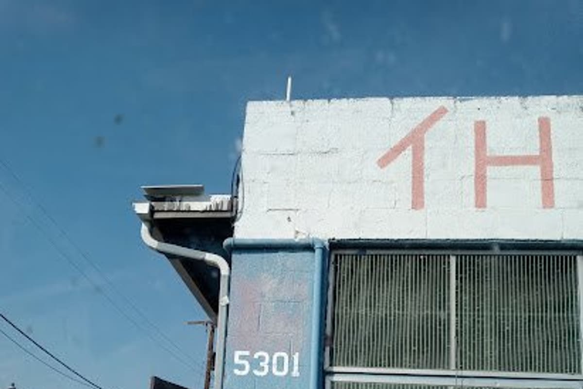 Bone Yard: Blue concrete block office building marked 5301 Office, with barred windows, an iron gate and a traffic cone under a clear sky