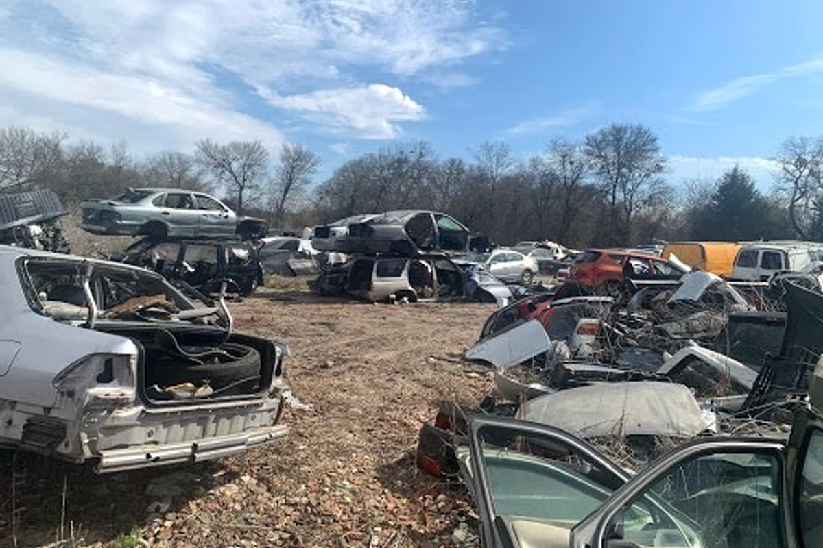 Experienced Auto Parts and Salvage: Wide view of a salvage yard with wrecked cars stacked and scattered across a dirt lot under a blue sky