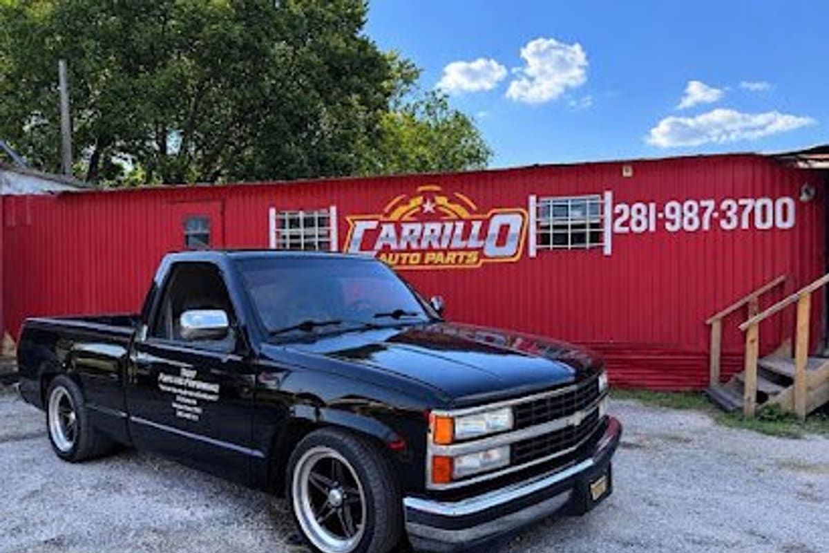 Carrillo Auto Parts: Red metal office building with a painted sign and phone number, a black pickup parked on gravel in front
