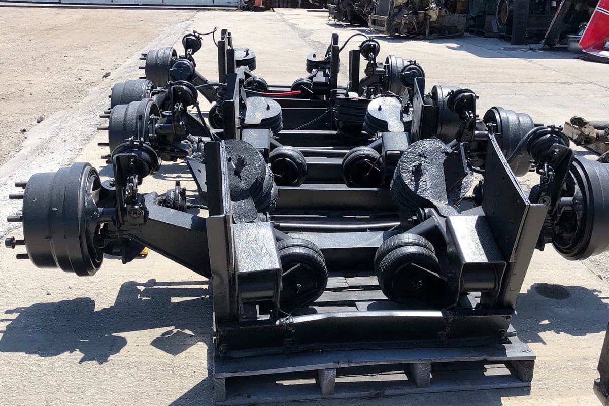 Ben Truck Parts: Rows of black truck axle and suspension assemblies on pallets in an outdoor salvage yard with other parts in the background