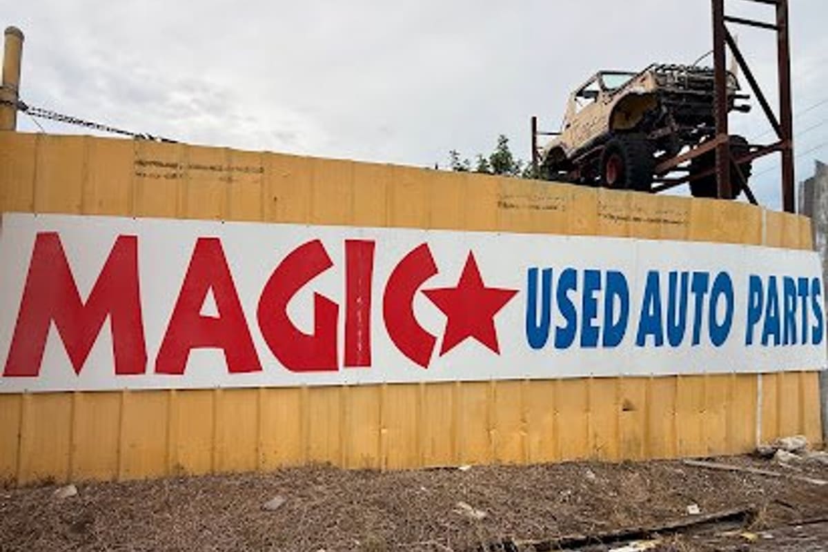 Majic Used Auto Parts: Large red, white and blue used auto parts sign on a yellow fence with a lifted off-road truck mounted above