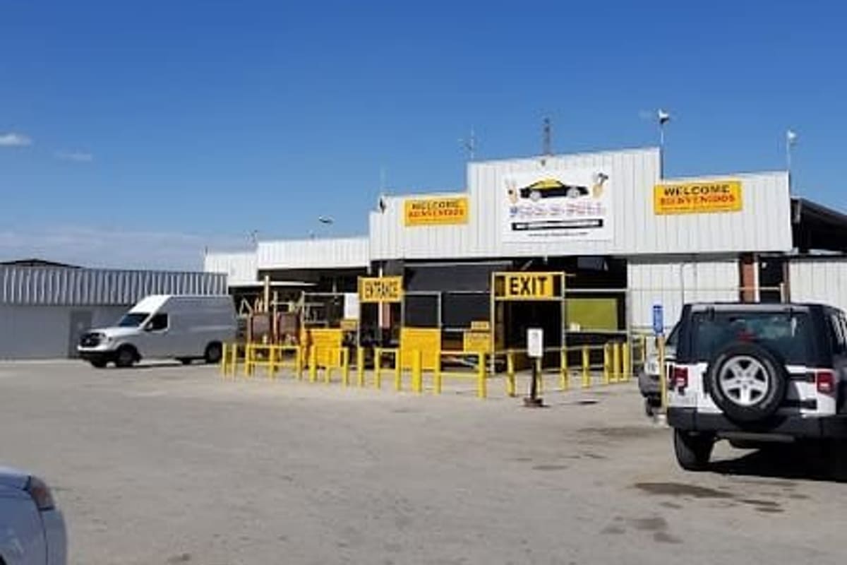 Pick and Pull Salvage Yard: Metal-roofed salvage yard building with yellow entrance and exit signs and a parking lot under a clear blue sky