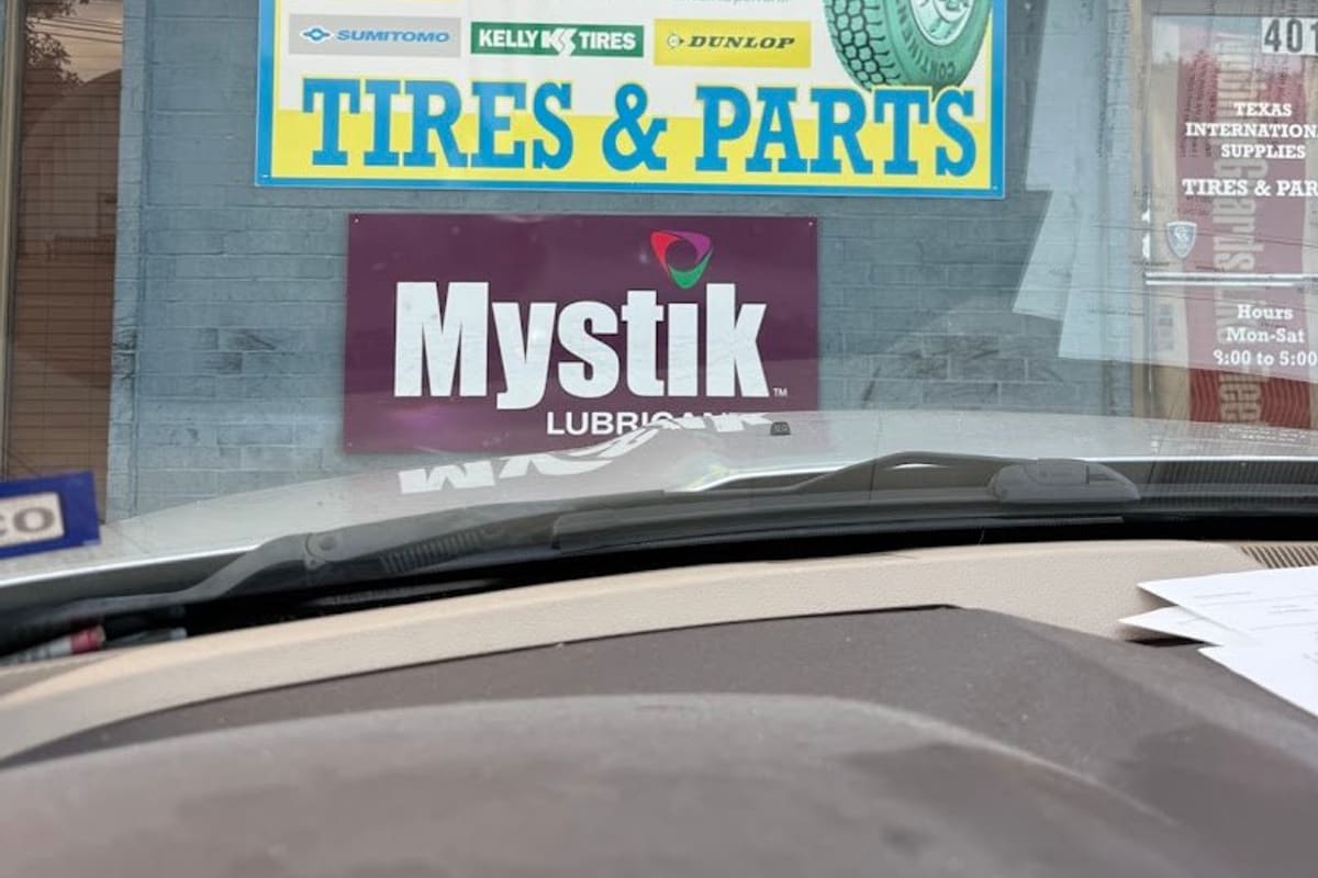 Texas International Tires Truck Parts & Chrome: Tires and Parts sign with tire brand logos on a gray brick storefront next to a door with posted hours