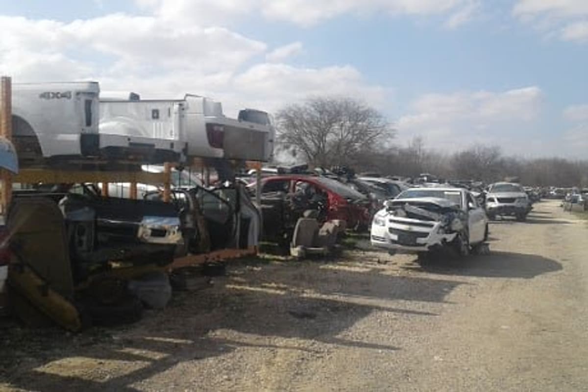 A-1 Salvage: Rows of wrecked cars and truck beds along a gravel lane in a salvage yard under a partly cloudy sky