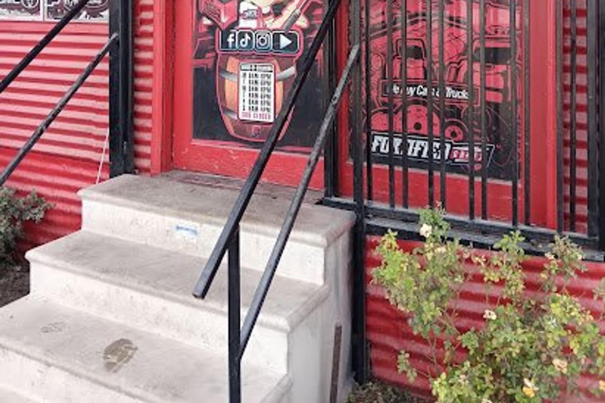 North-Jensen Auto Parts: Red corrugated building entrance with concrete steps, black railings, a red door and a barred window covered in posters