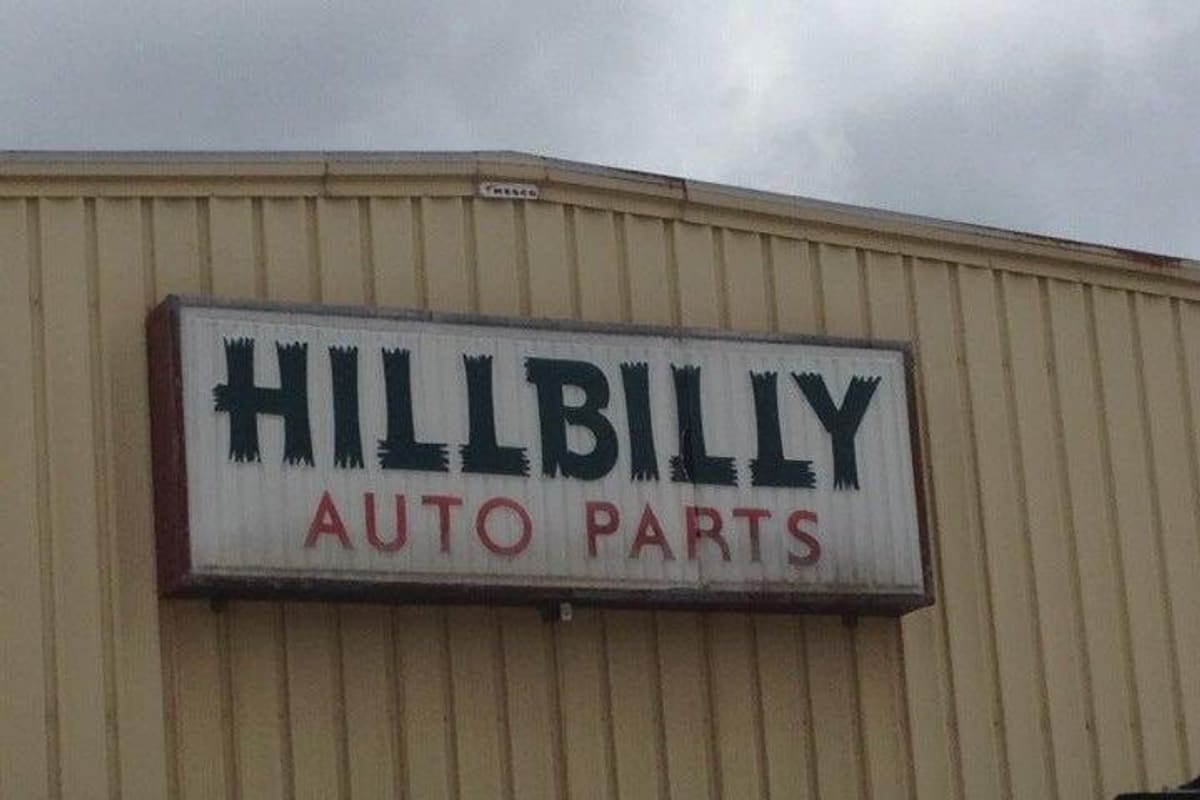 Hillbilly Auto Parts: White signboard reading Hillbilly Auto Parts mounted on a tan metal building under a cloudy sky